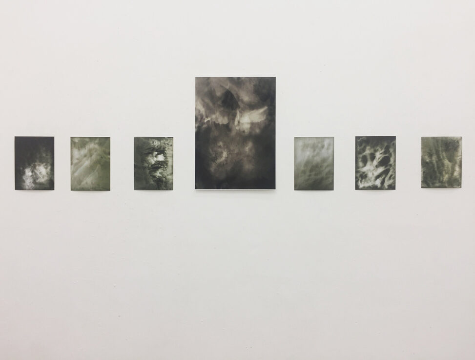 Photograph of a gallery wall with 7 black and white images on it.