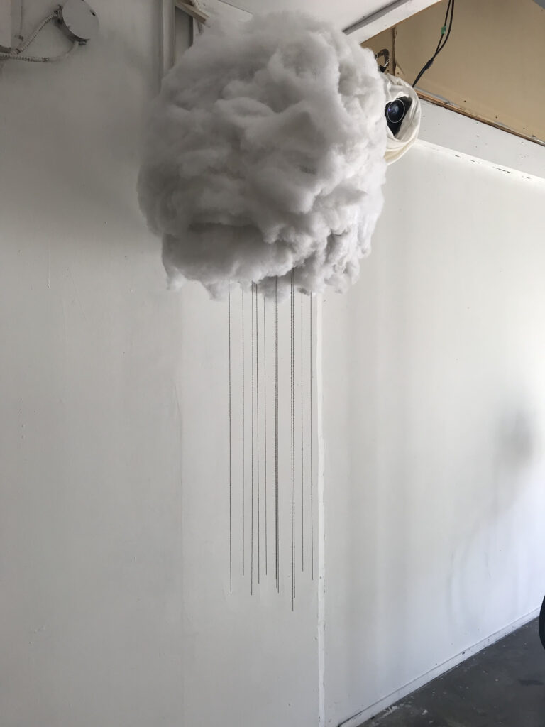 Soft sculpture of a small cloud, it appears to be raining.